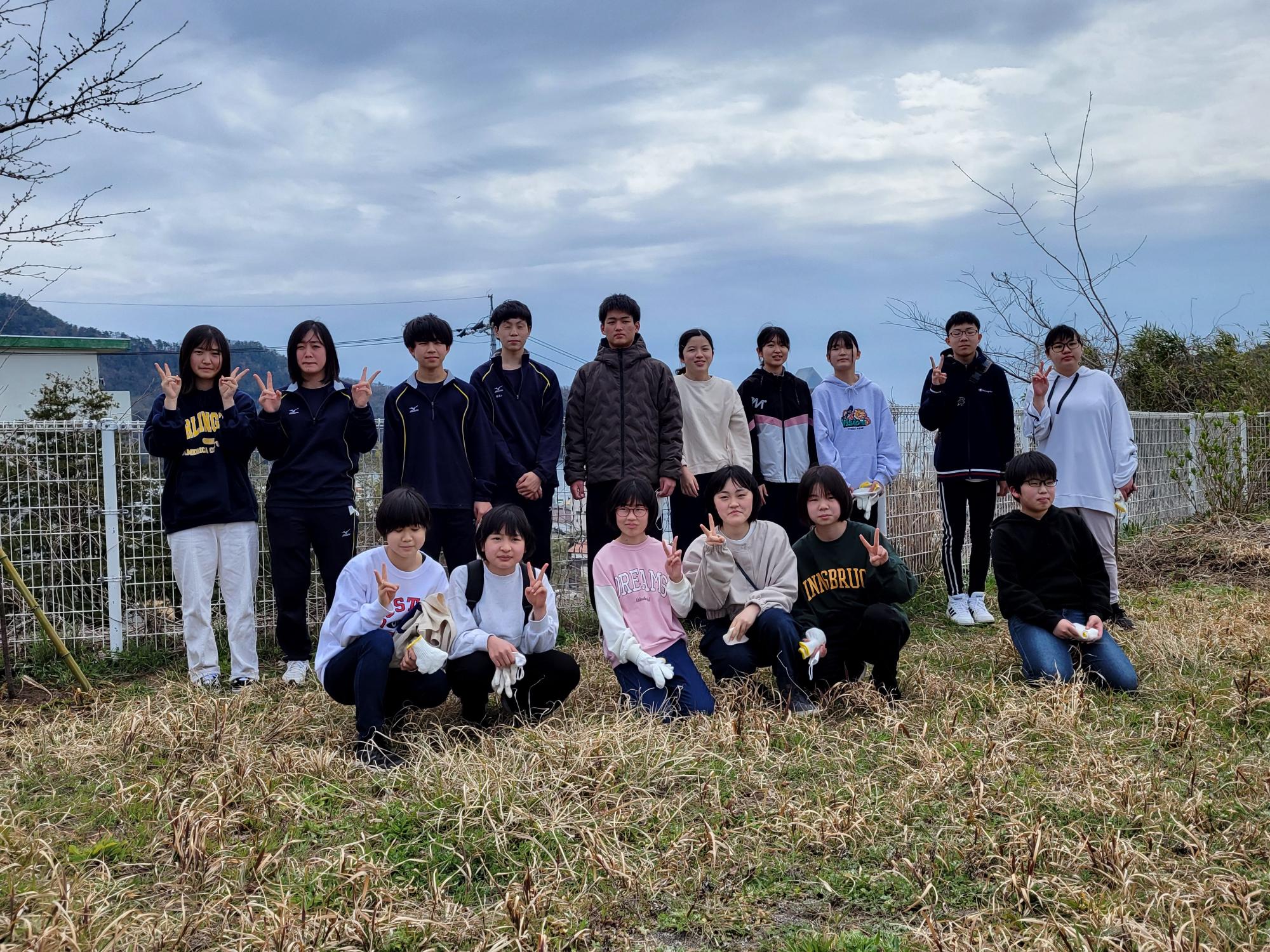 曇天を背景に、公園で集まり各々ピースサインや笑顔を見せる生徒達の集合写真