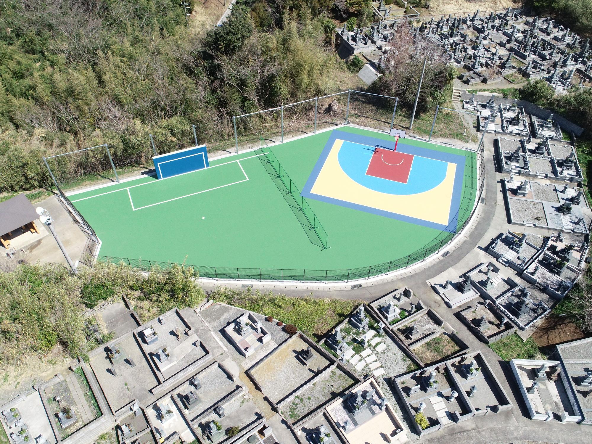 多数のお墓のある土地と木々の土地に接した不規則な形の運動広場の写真