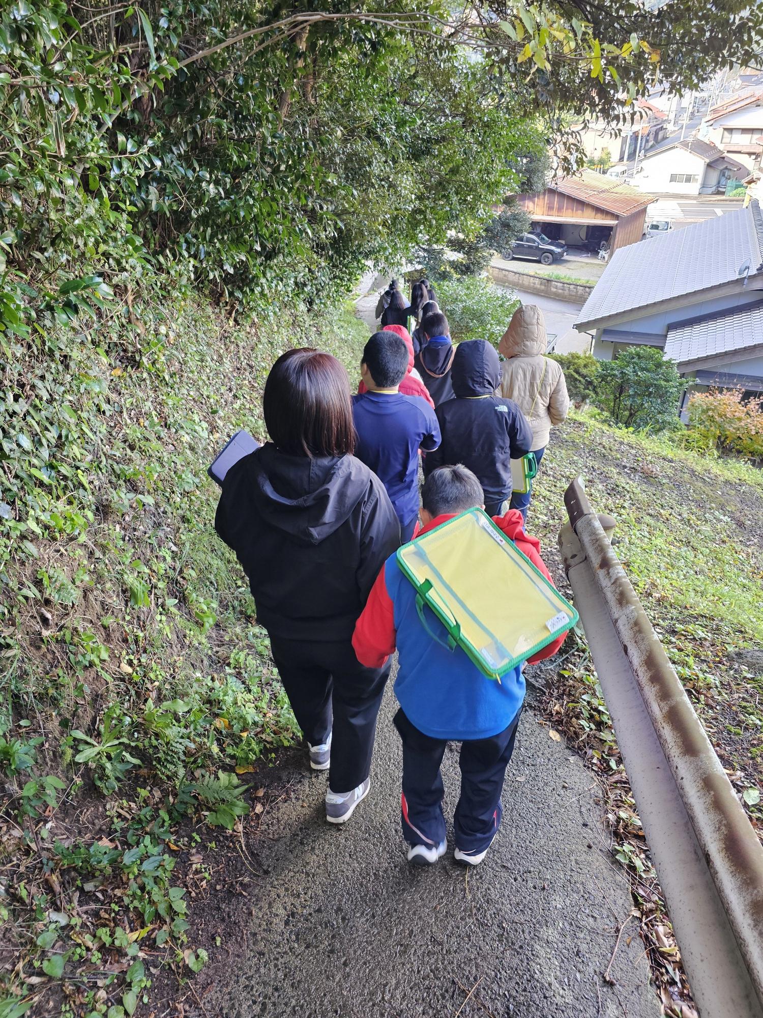 列になった子どもたちが狭い道の斜面を下っている写真