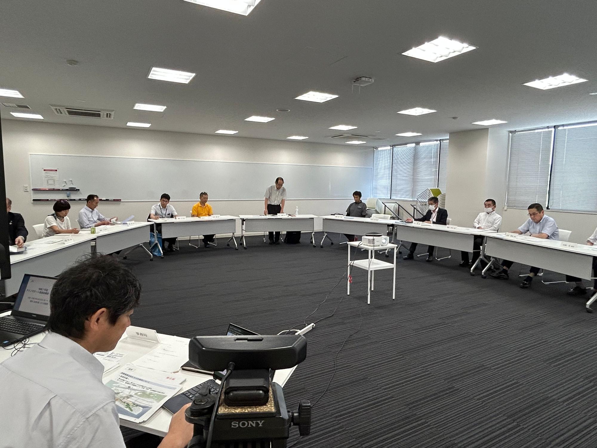 円形に並んだ席に座って会議をする人々の写真