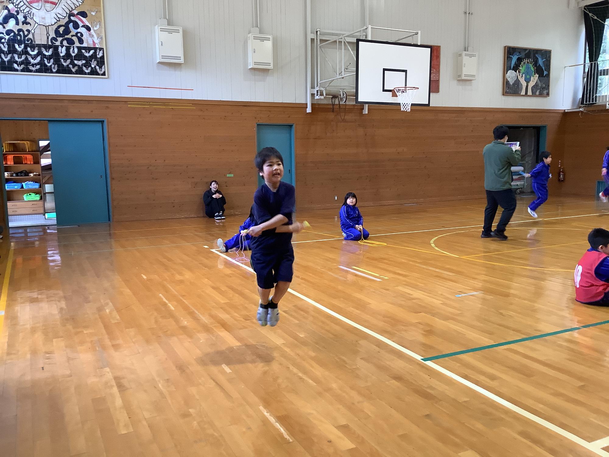 なわとび大会にて、体育館で自分で回している縄を跳ぶ男子生徒の様子が映った写真