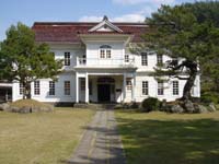 真ん中にまっすぐの小道があり、赤い屋根とシンメトリーな構造が特徴的な隠岐郷土館の写真