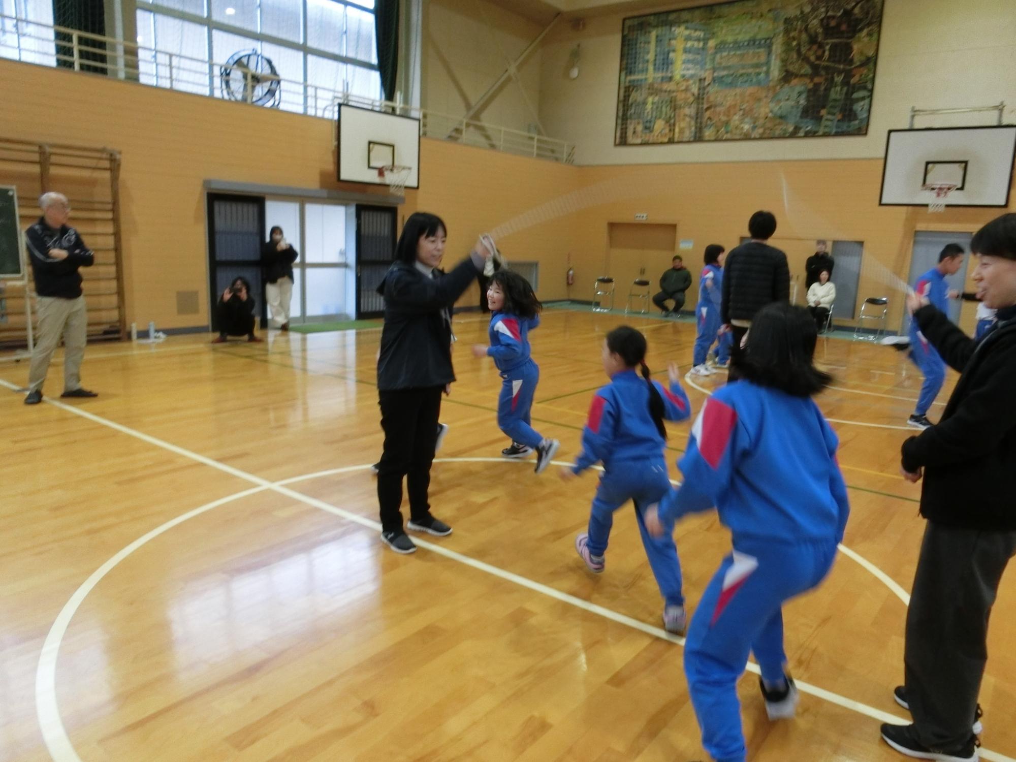 体育館で縄跳びを回す教職員と跳ぶ子供たちが映った写真