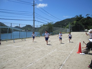 鮮やかな青空の下、校庭に書かれた白いトラックを全力疾走する児童たちの写真