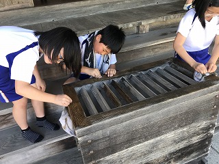 神社で児童3人が雑巾を使い真剣な表情で賽銭箱を清掃している写真