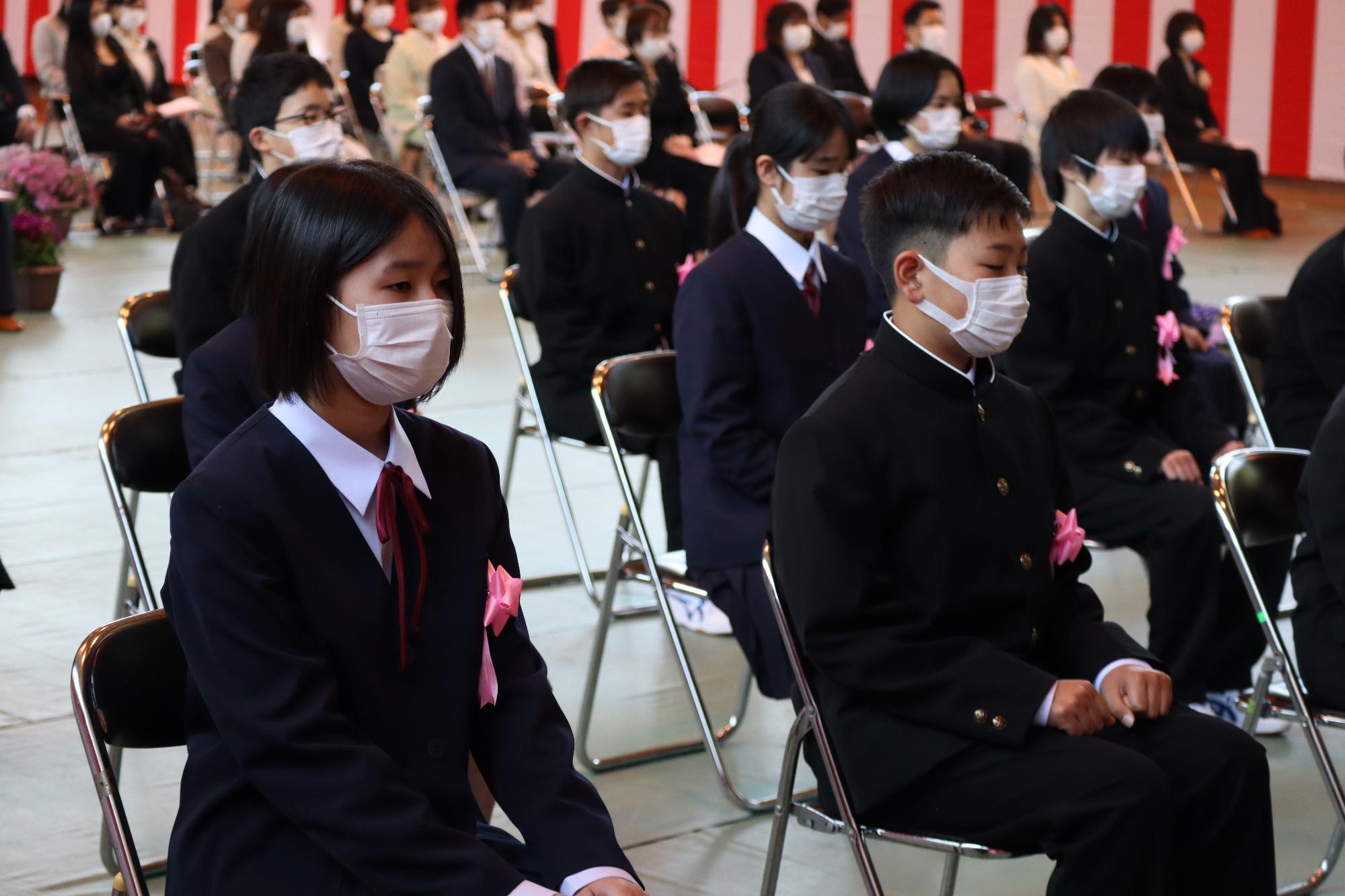 紅白幕が掛けられた体育館で沢山の保護者の方々が見守る中、少し緊張した面持ちで入学式に望む新入生の写真