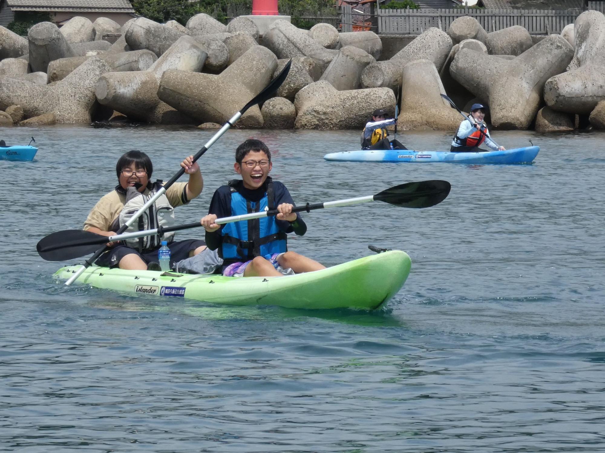 黄緑色のカヤックに乗り、満面の笑みでオールを漕ぐ2人の男子生徒の写真