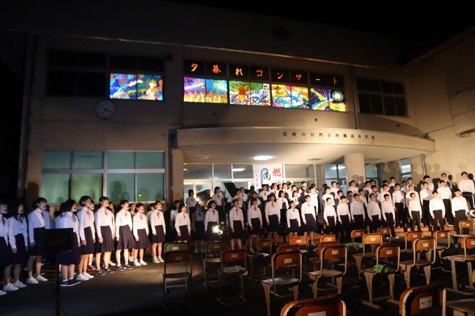 昇降口前で行われた「夕暮れコンサート」で合唱する生徒たちの写真