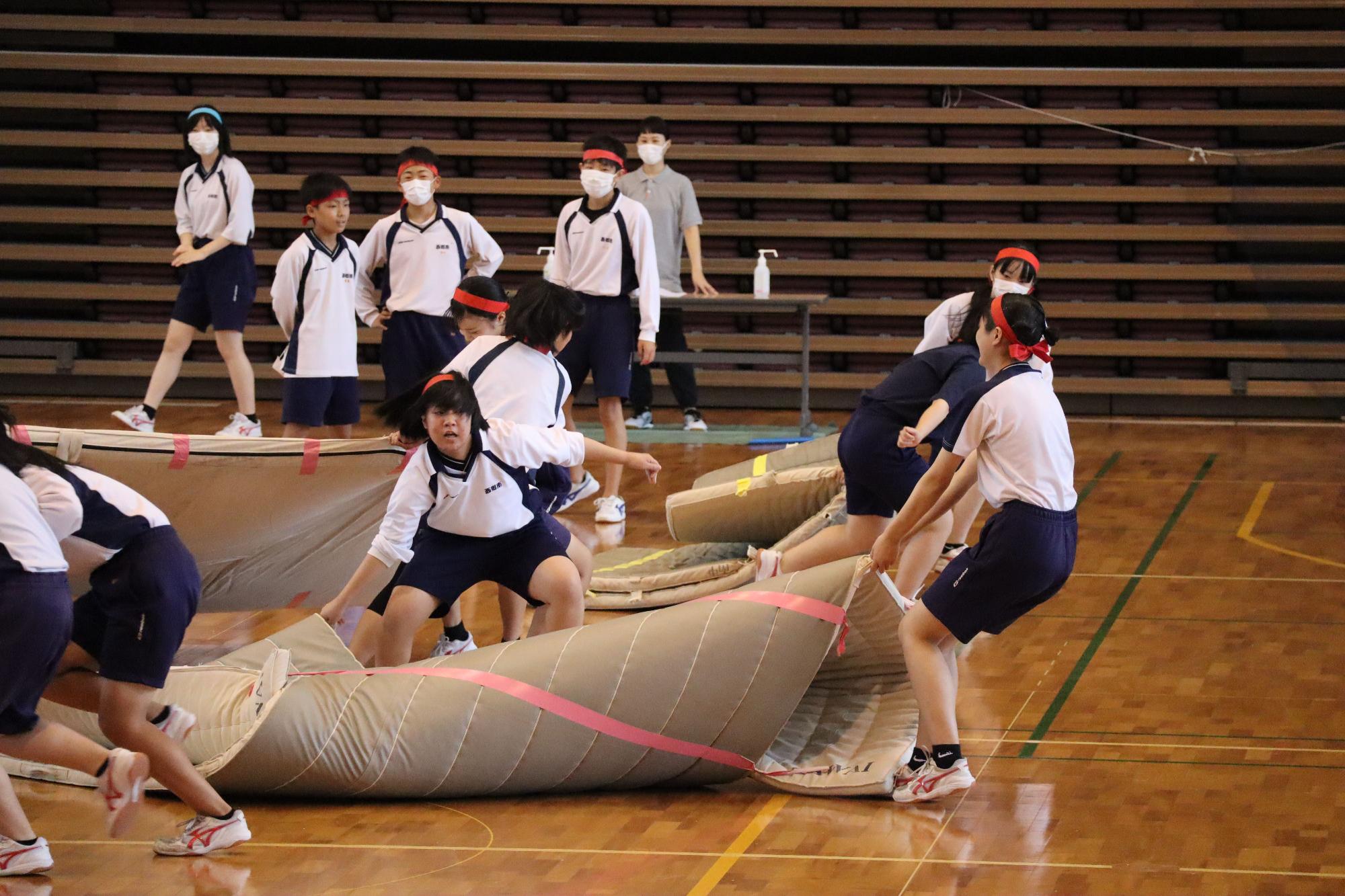 体育館でチームごとにマットを運び競い合う生徒たちの写真