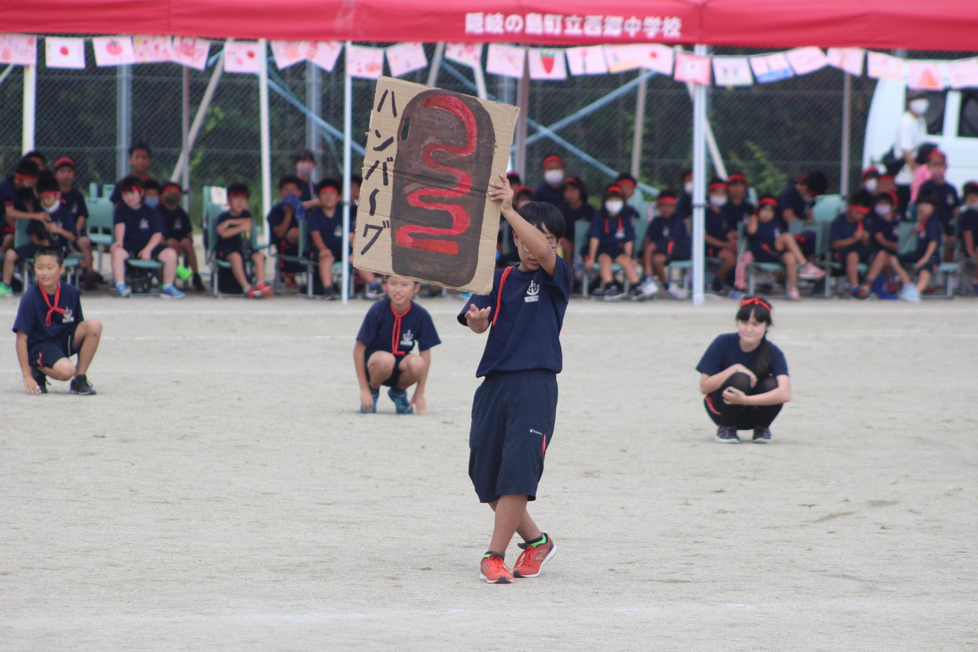 校庭でハンバーグのイラスト看板を掲げて盛り上げる生徒の写真