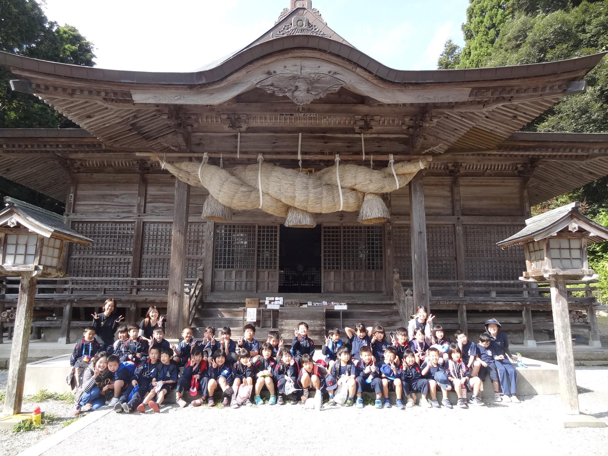 大きなしめ縄の飾られた神社の境内の前で生徒たちが集合して記念撮影する写真