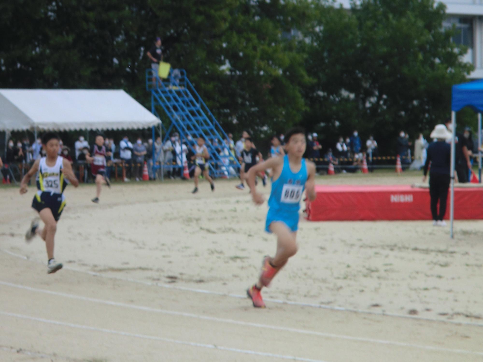 陸上大会でそれぞれのチームのユニフォームを着てトラックを力強く走る選手たちの写真
