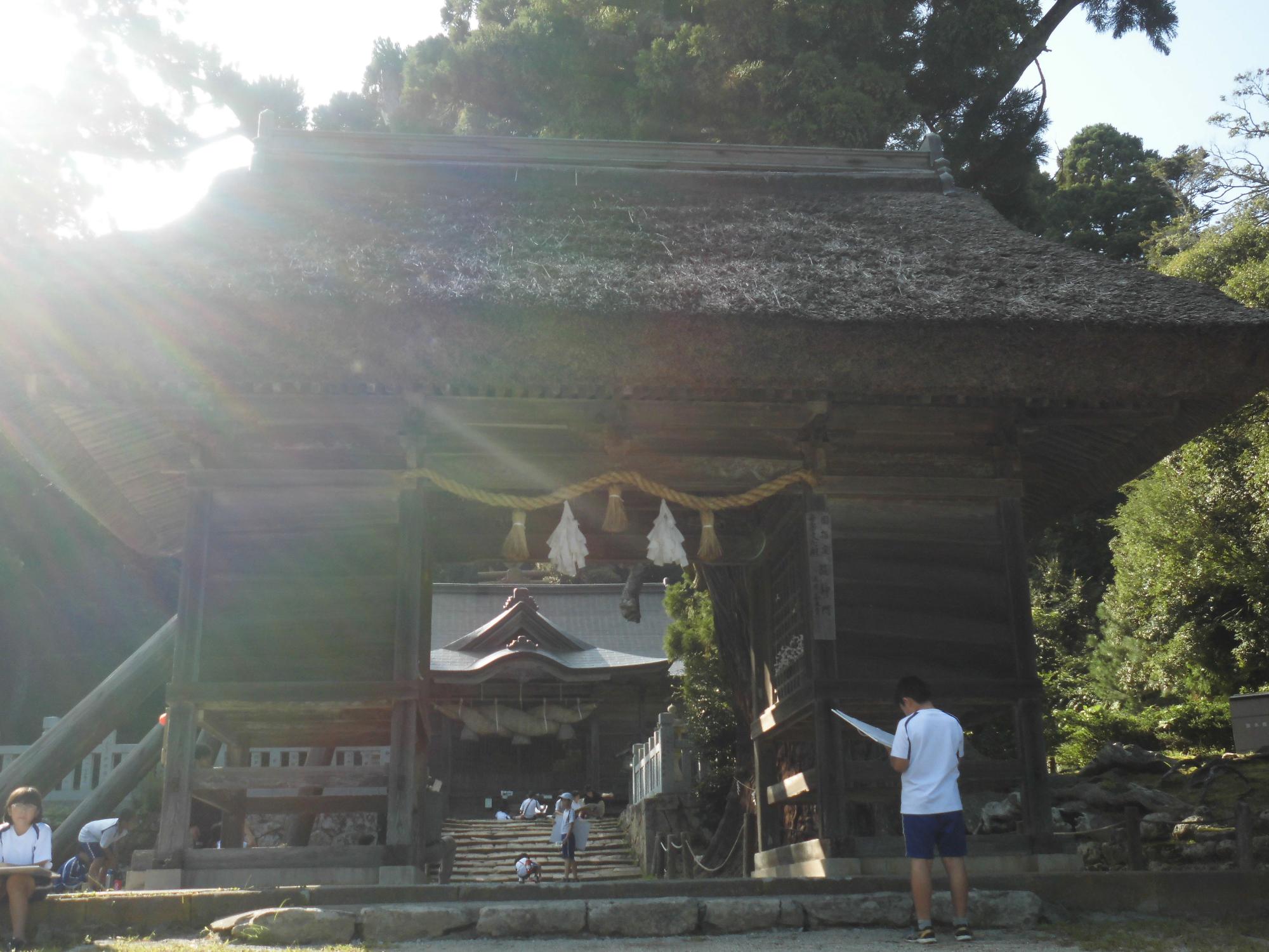 玉若酢神社の瓦葺き屋根が特徴的な大きな門を立って写生している男の子の写真