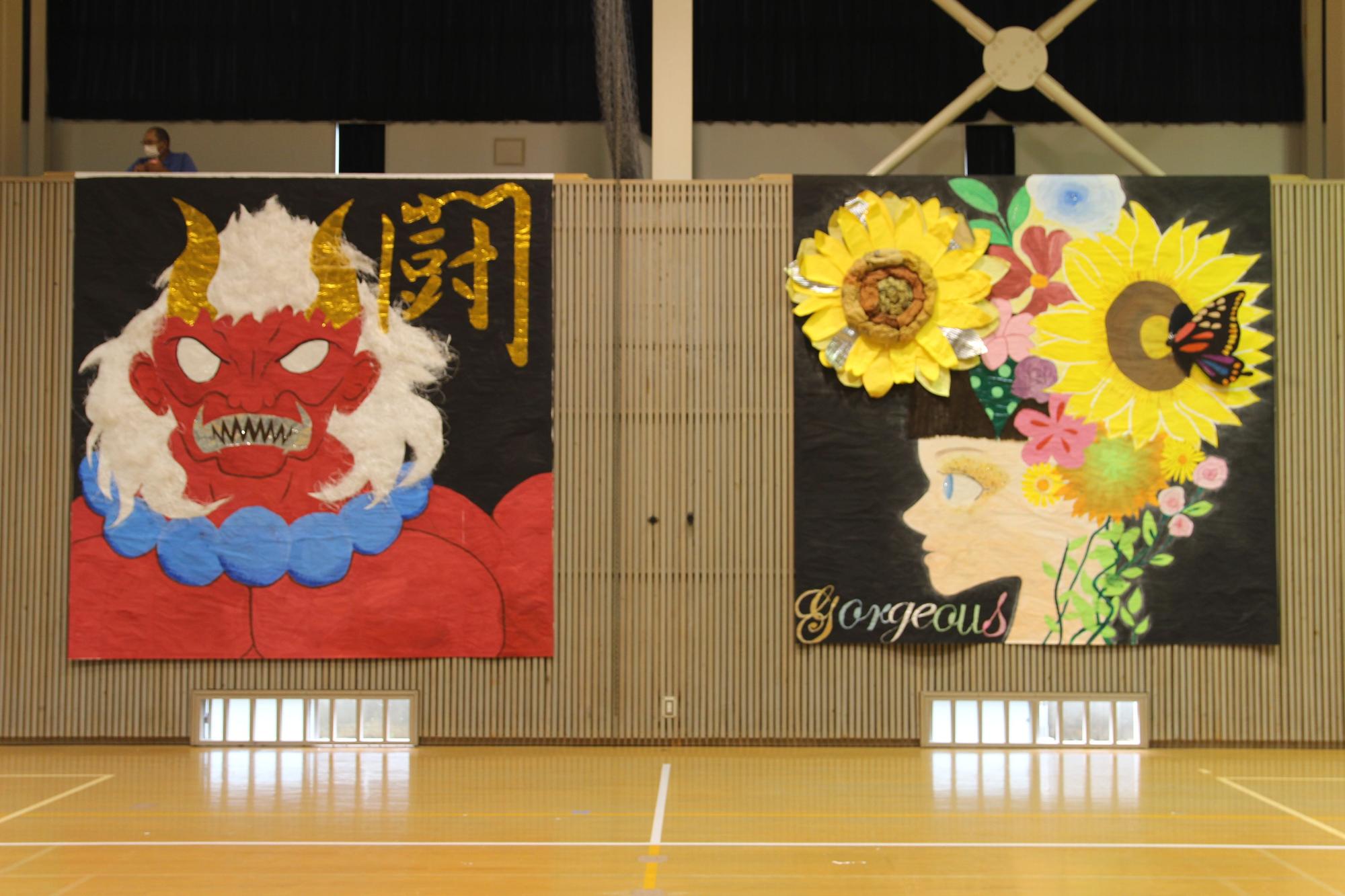 体育館の壁に飾られた鬼のイラストと黄色い花が頭に咲いている人の横顔のイラストが大きく並んでいる写真
