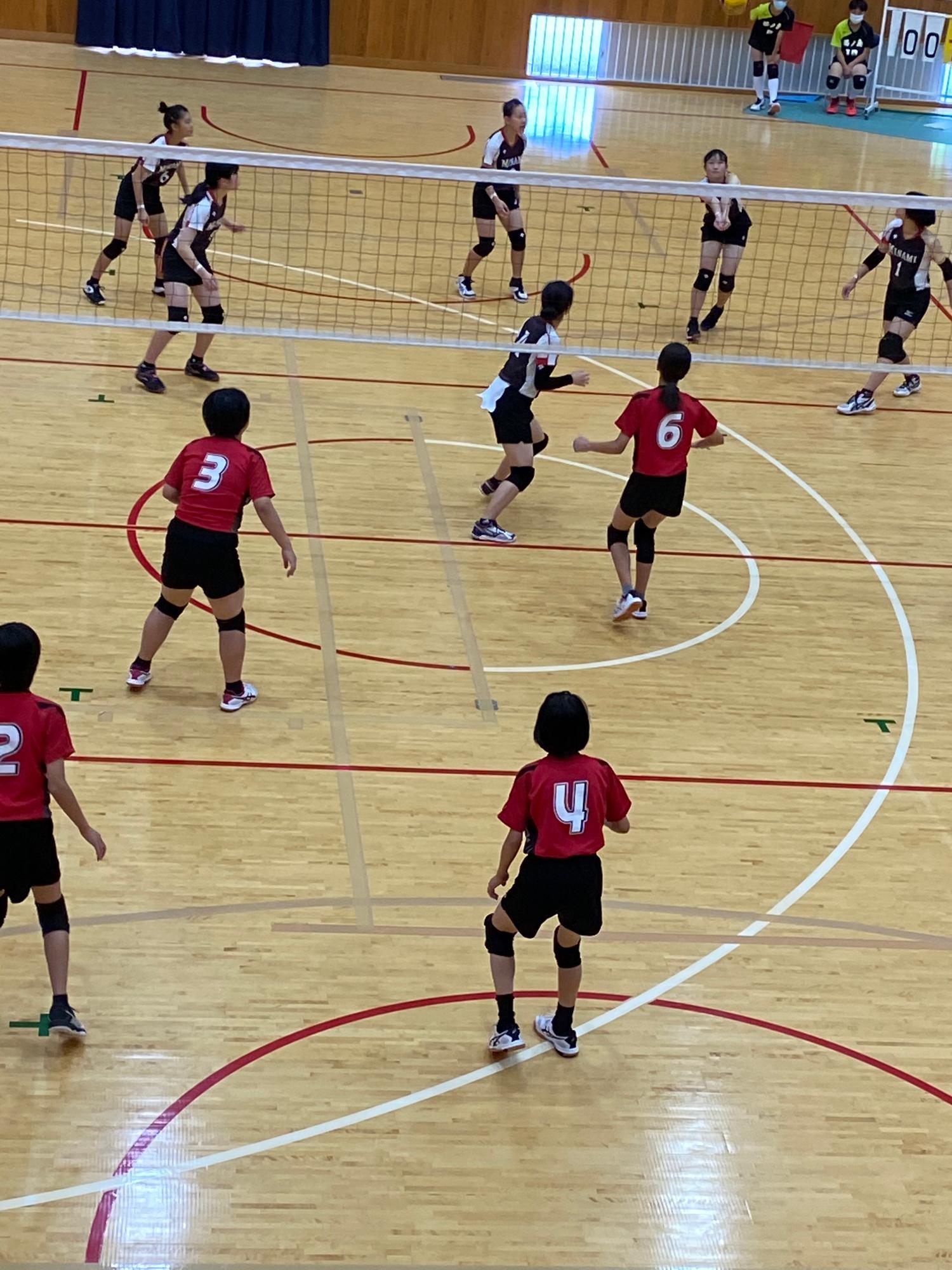 体育館で赤いユニフォームを着たバレーボール試合をする生徒たちの写真
