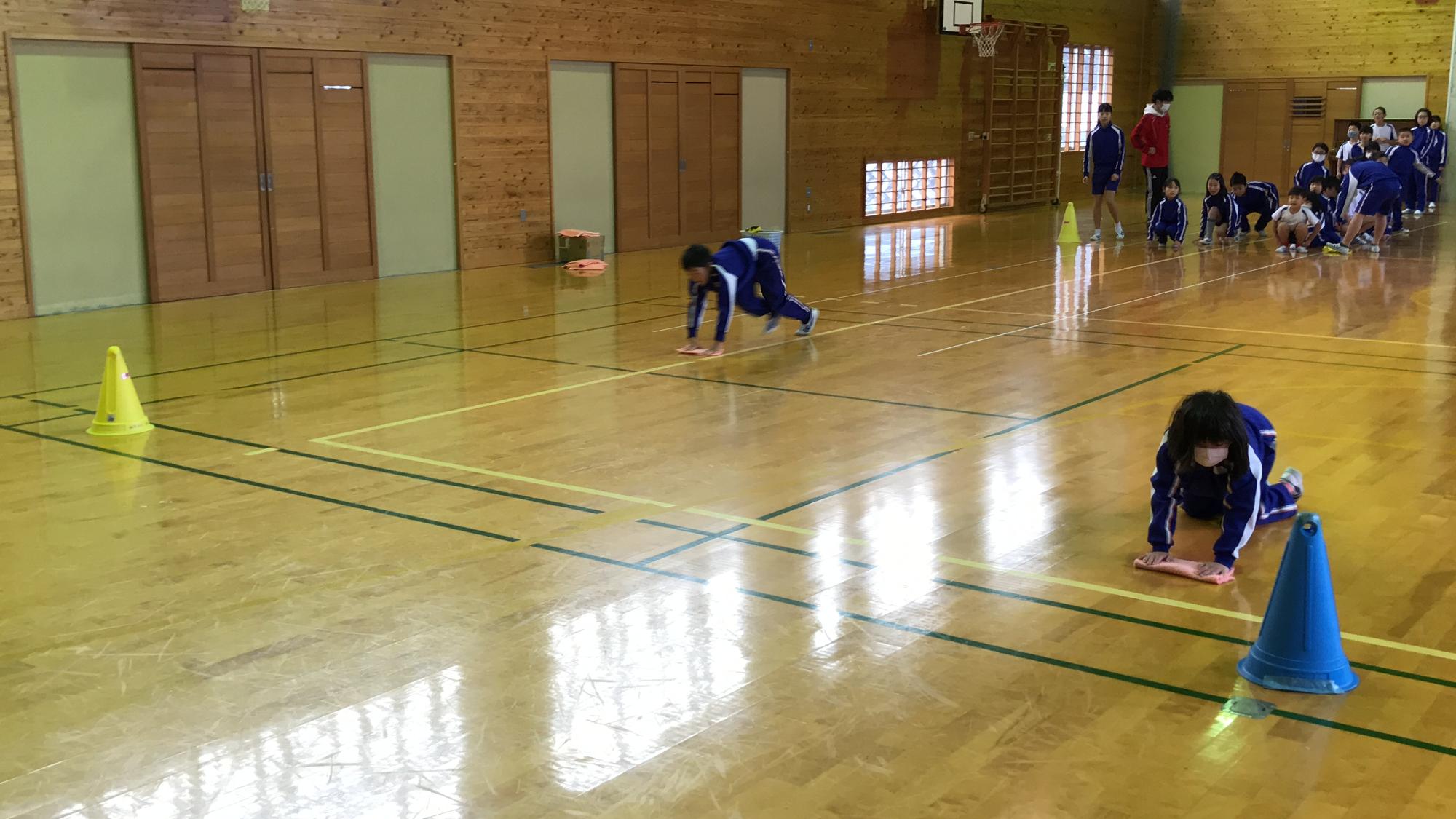 体育館で児童たちが雑巾がけ競争をしている写真