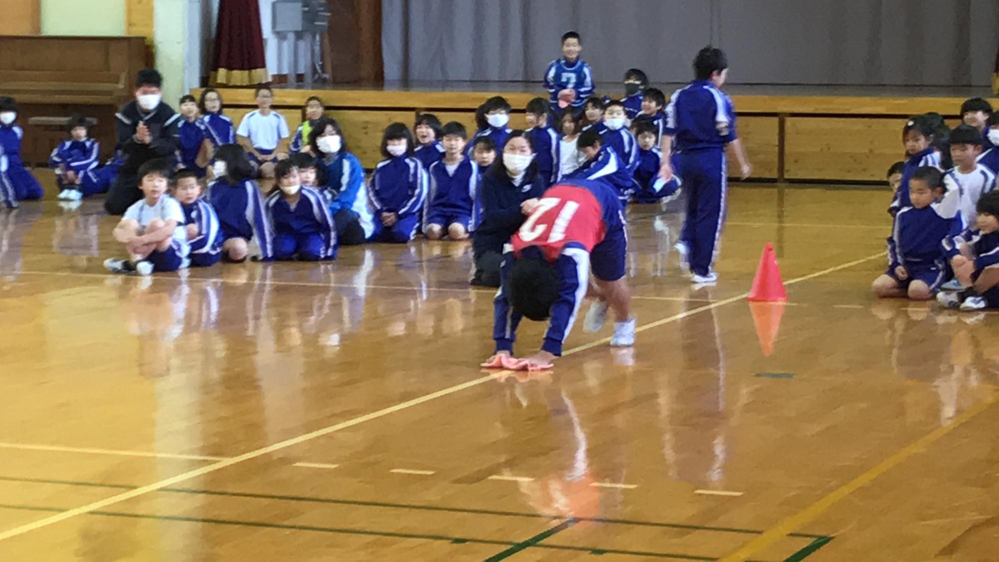 体育館で児童たちが応援しながら雑巾リレーをしている写真