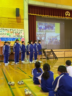 体育館で児童たちがスクリーンを使って発表を行っている写真