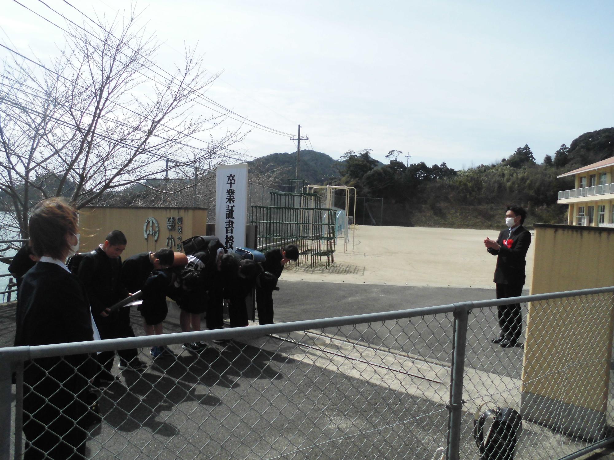 校門前で中学制服を着た児童たちが頭を下げてお辞儀をしている写真
