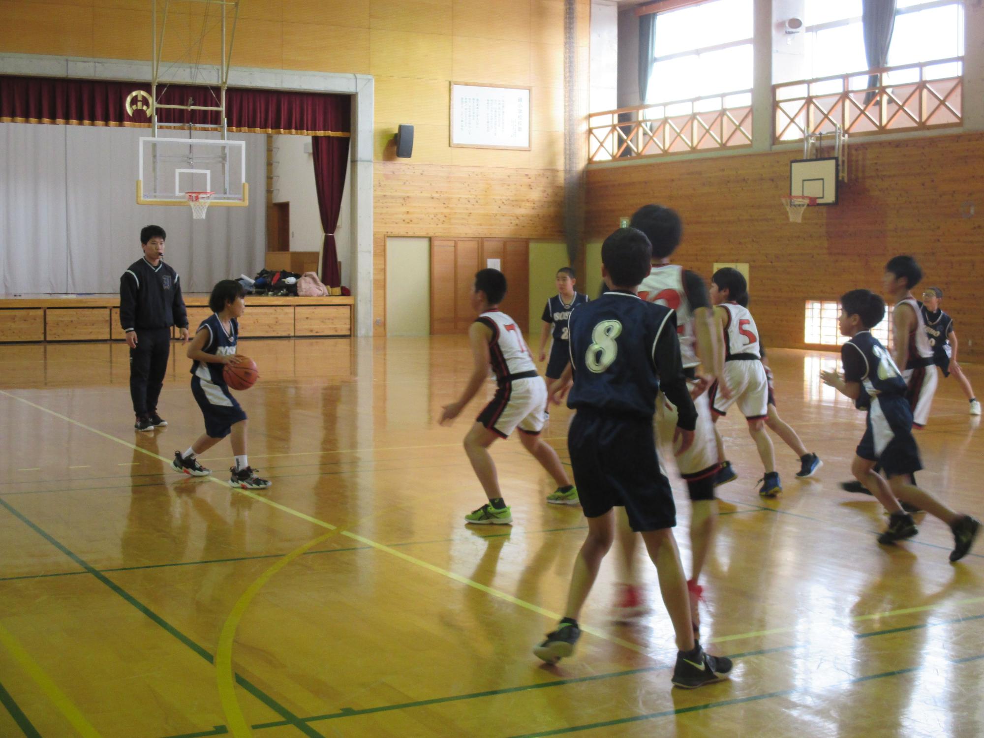 体育館で児童たちがバスケットボールの試合をしている写真
