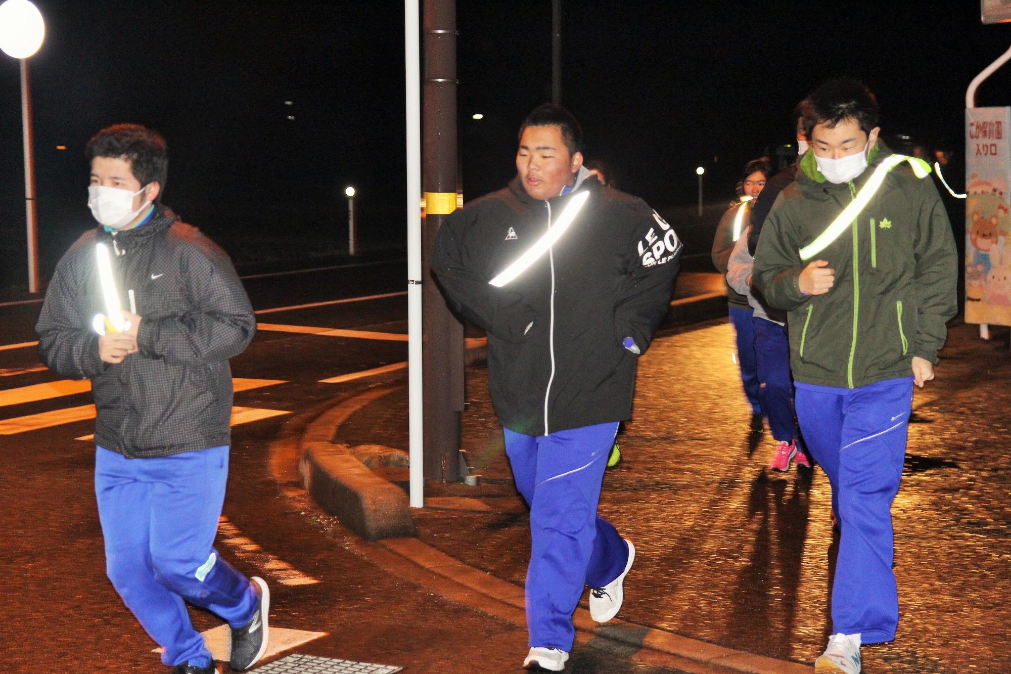夜の道路を反射板をつけて歩いている生徒たちの写真
