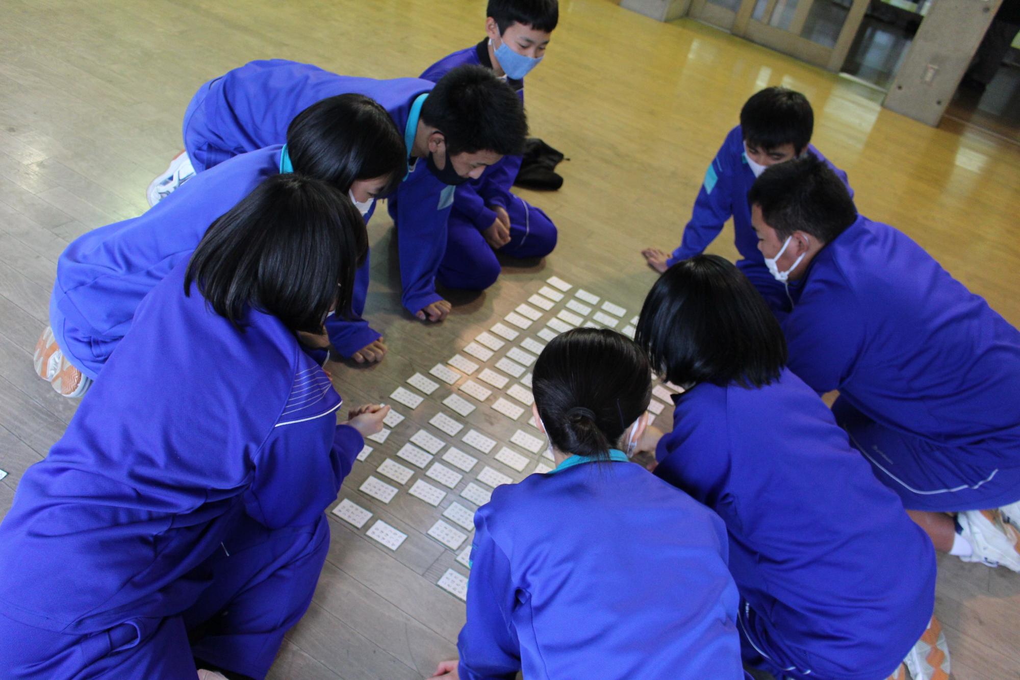体育館で生徒たちがかるたを囲んでいる写真