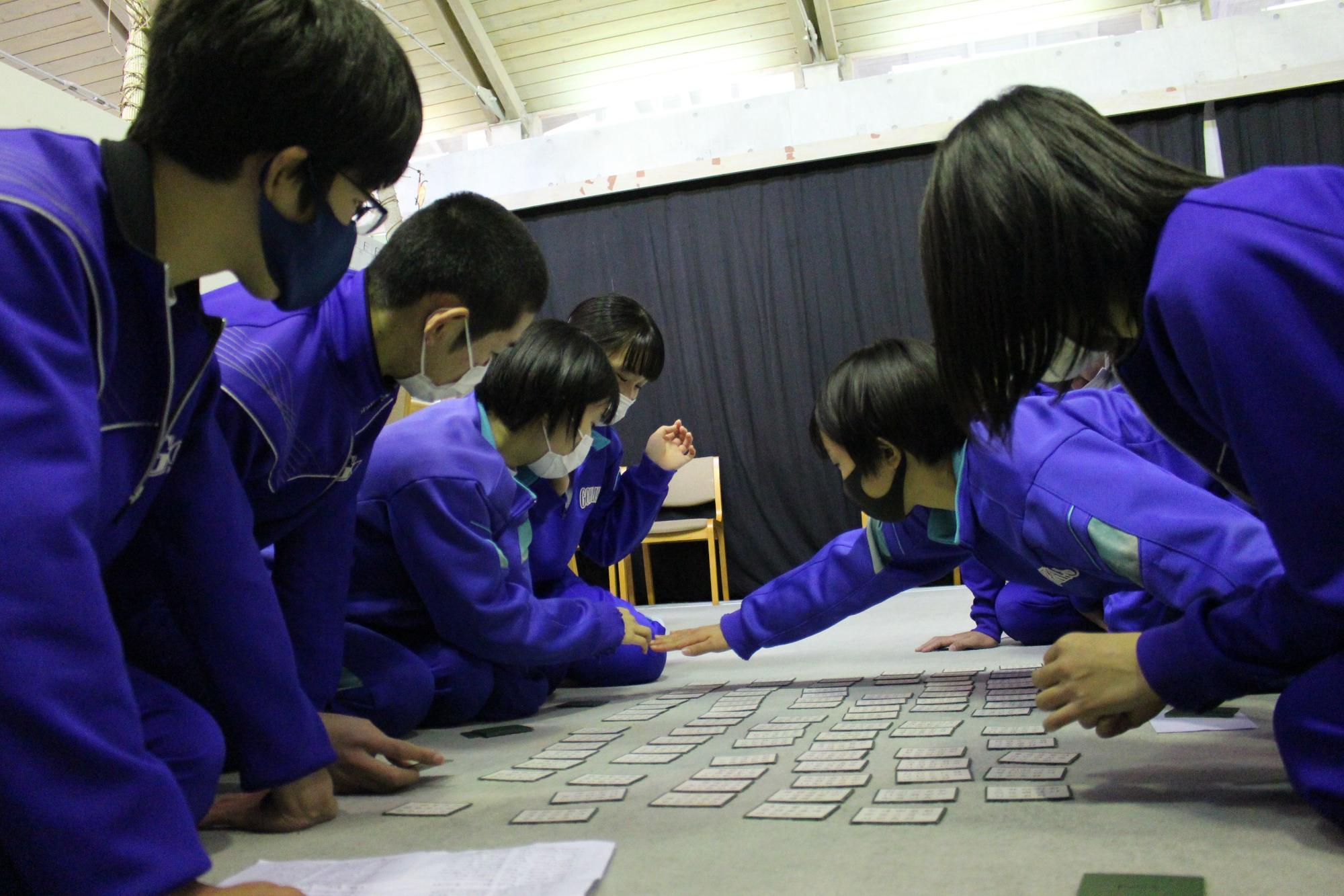 室内で生徒たちがかるたを取る瞬間の写真