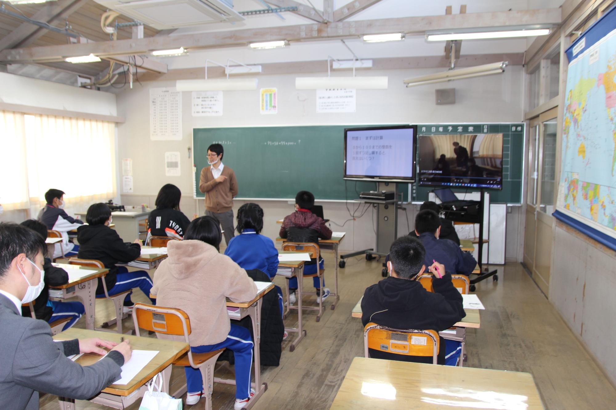 教室で先生の話を聞きながら生徒たちが授業を受けている写真