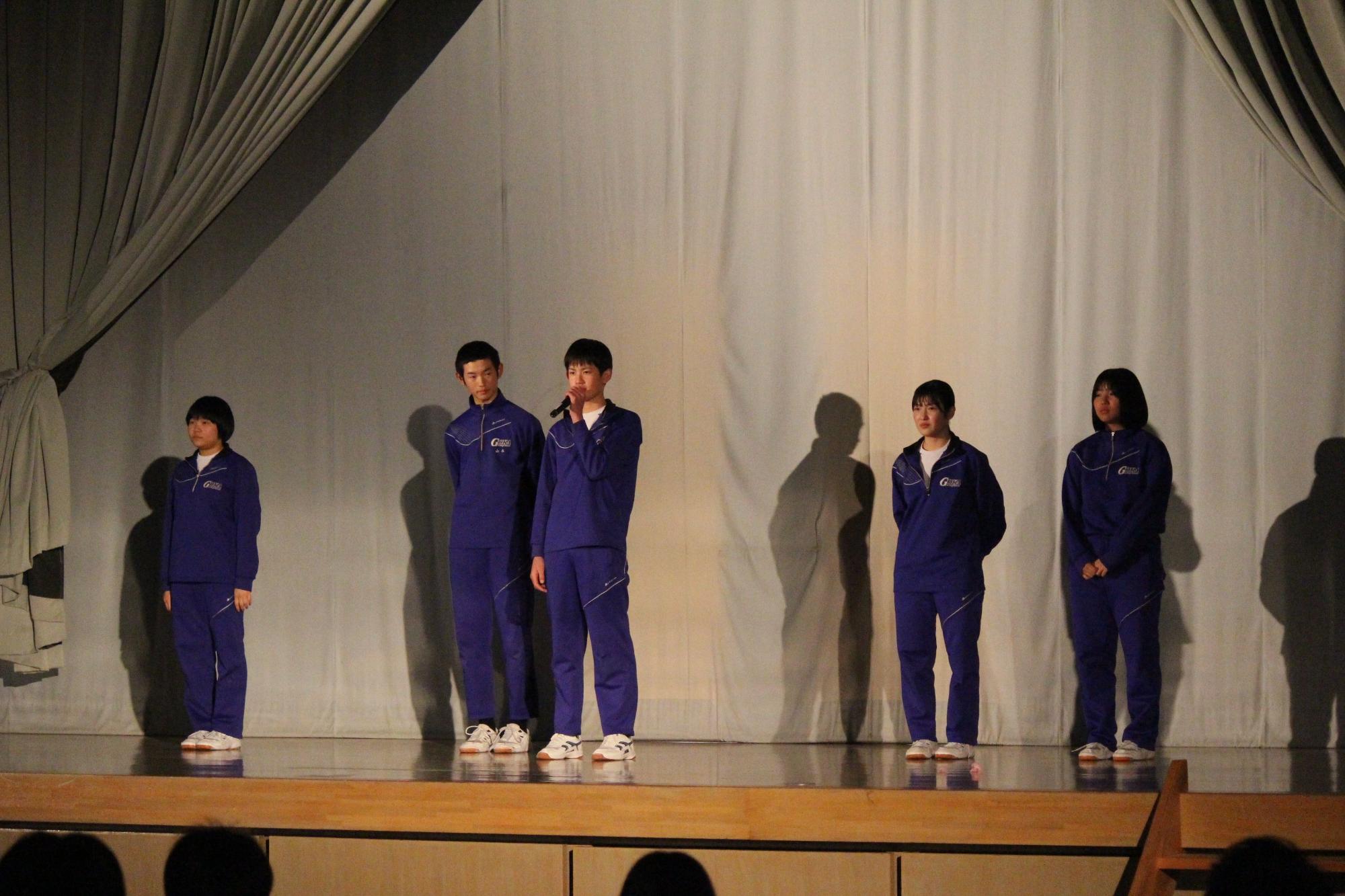 ステージ上で生徒がマイクを持って話している写真