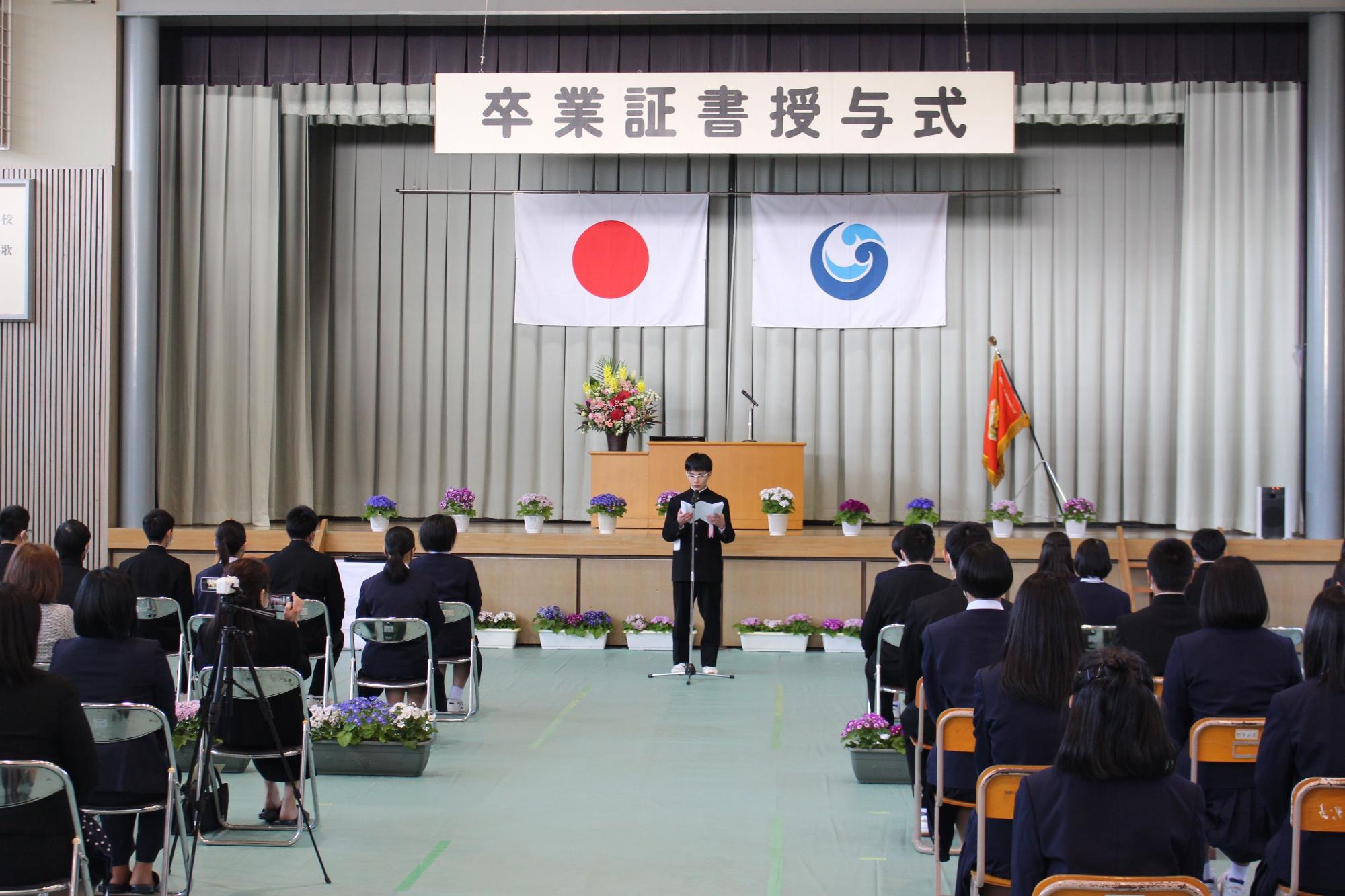 体育館で卒業式が行われ、生徒がスピーチをしている写真