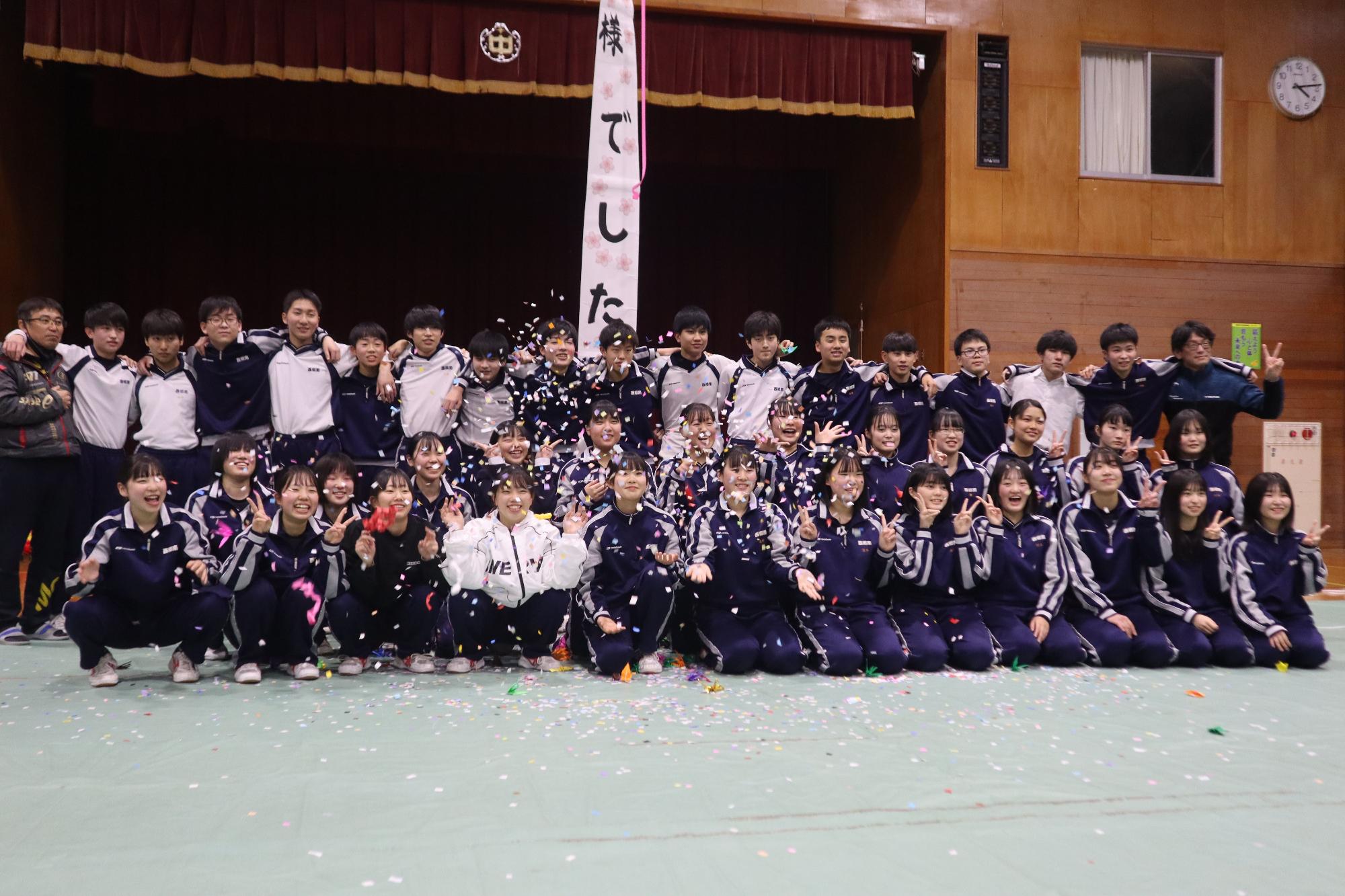 体育館で生徒たちが笑顔で集合写真を撮っている写真