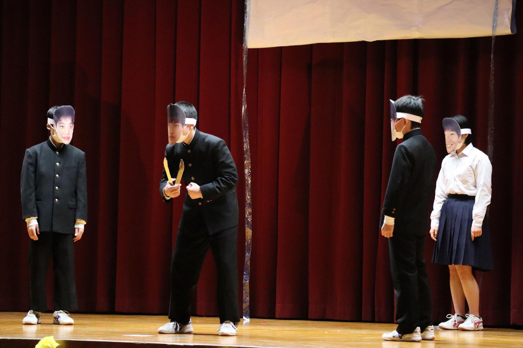 舞台でお面をつけた生徒4人が寸劇をしている写真