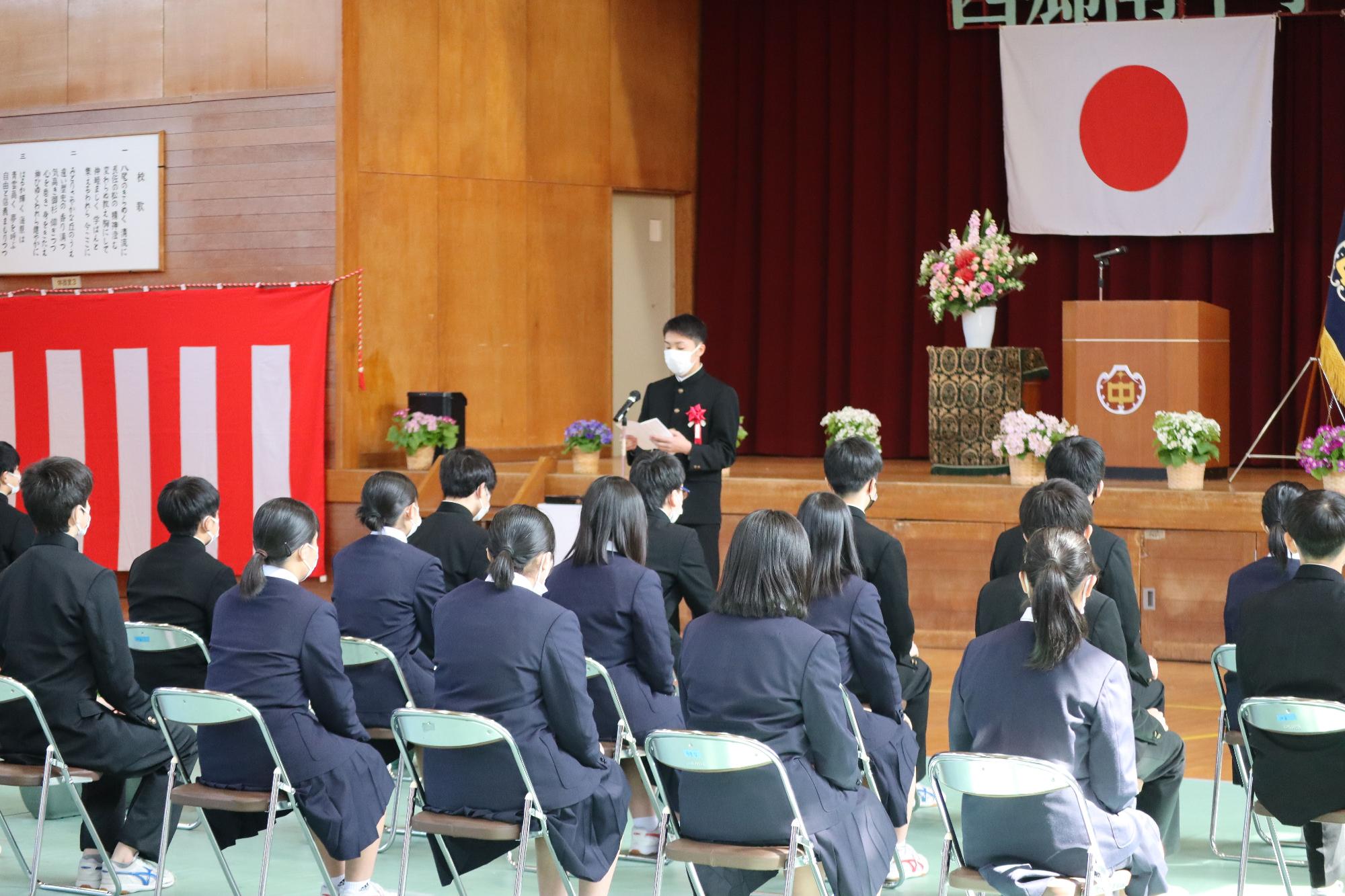 体育館で行われた卒業式で卒業生代表が立って答辞を述べている写真