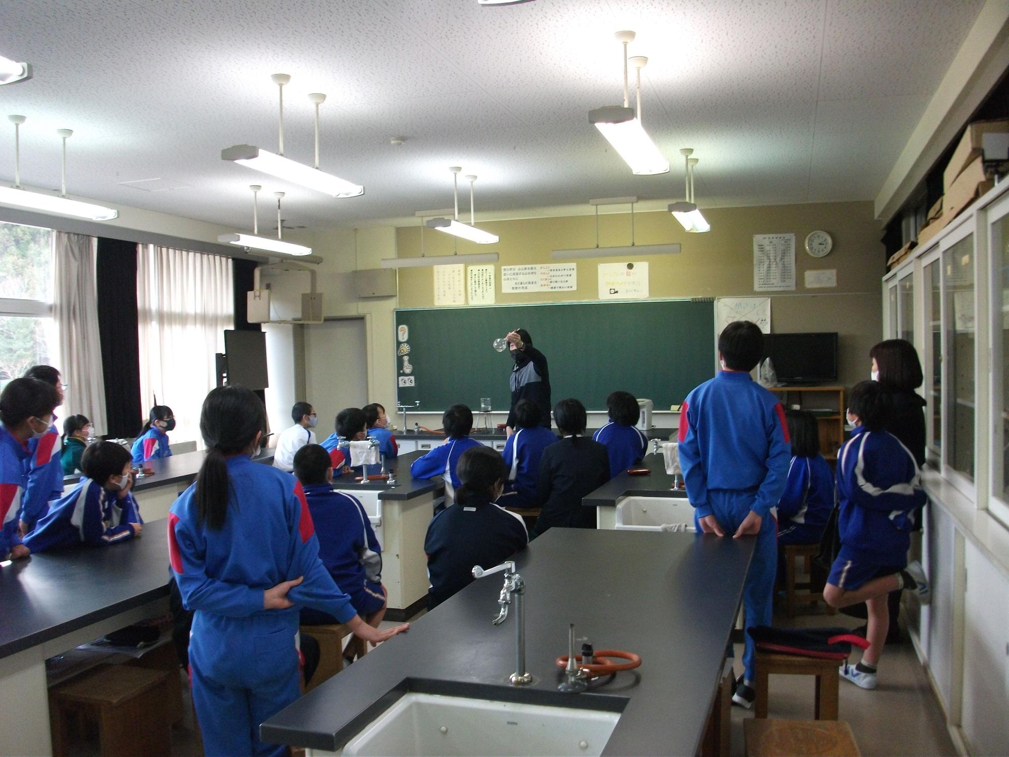 ジャージ姿の生徒たちが理科室のような場所で授業を受けている写真