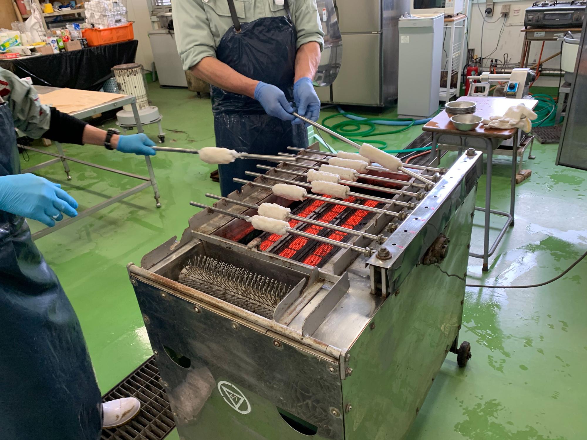 実習室で職員の方2人がマシンを使いちくわを焼いている写真