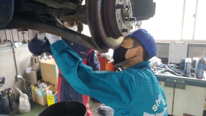 整備工場で作業着を着た生徒が車の下部を点検している写真