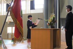 体育館の壇上で生徒が証書を読み上げている入学式の写真