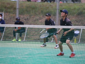 テニスコートで男子生徒たちがダブルスの試合に臨んでいる写真