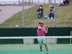 テニスコートで女子生徒がバックハンドでボールを打ち返している写真