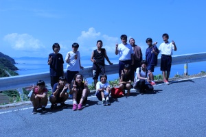 海沿いの坂道で青空を背景に並んで記念撮影をする生徒たちの写真