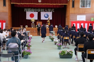 体育館の舞台前で新入生が入場している入学式の様子の写真