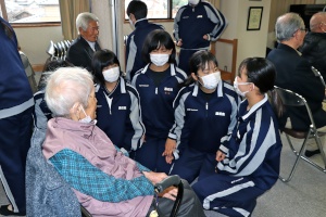 老人ホームで椅子に座り、一人の高齢女性と話をしている4人の女子生徒の写真