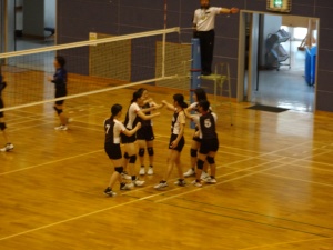 体育館で女子がハイタッチをしている様子のバレーボールの試合の写真