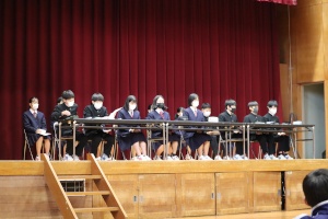 体育館の舞台上で生徒会の生徒たちが並んで座っている様子の写真