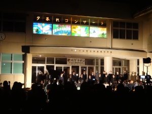 昇降口前で催された夕暮れコンサートで沢山の観客の前で合唱する生徒たちの写真