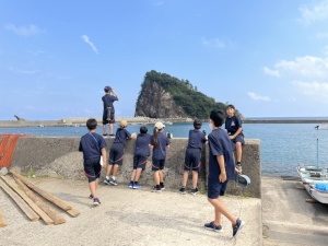 港の堤防で児童たちが海を眺めている写真