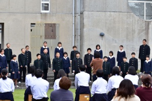 校庭で児童生徒たちが合唱を披露する様子の写真