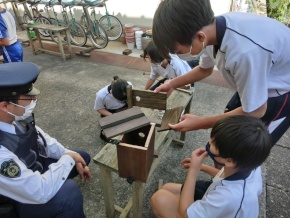 校庭で警察官と児童たちが巣箱作りを行っている写真