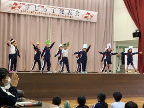 体育館の舞台で帽子をかぶった児童たちが発表している写真