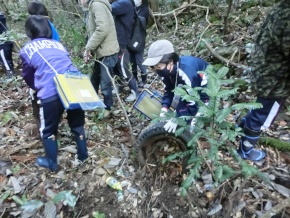 森の中でごみ拾いをする児童たちの写真